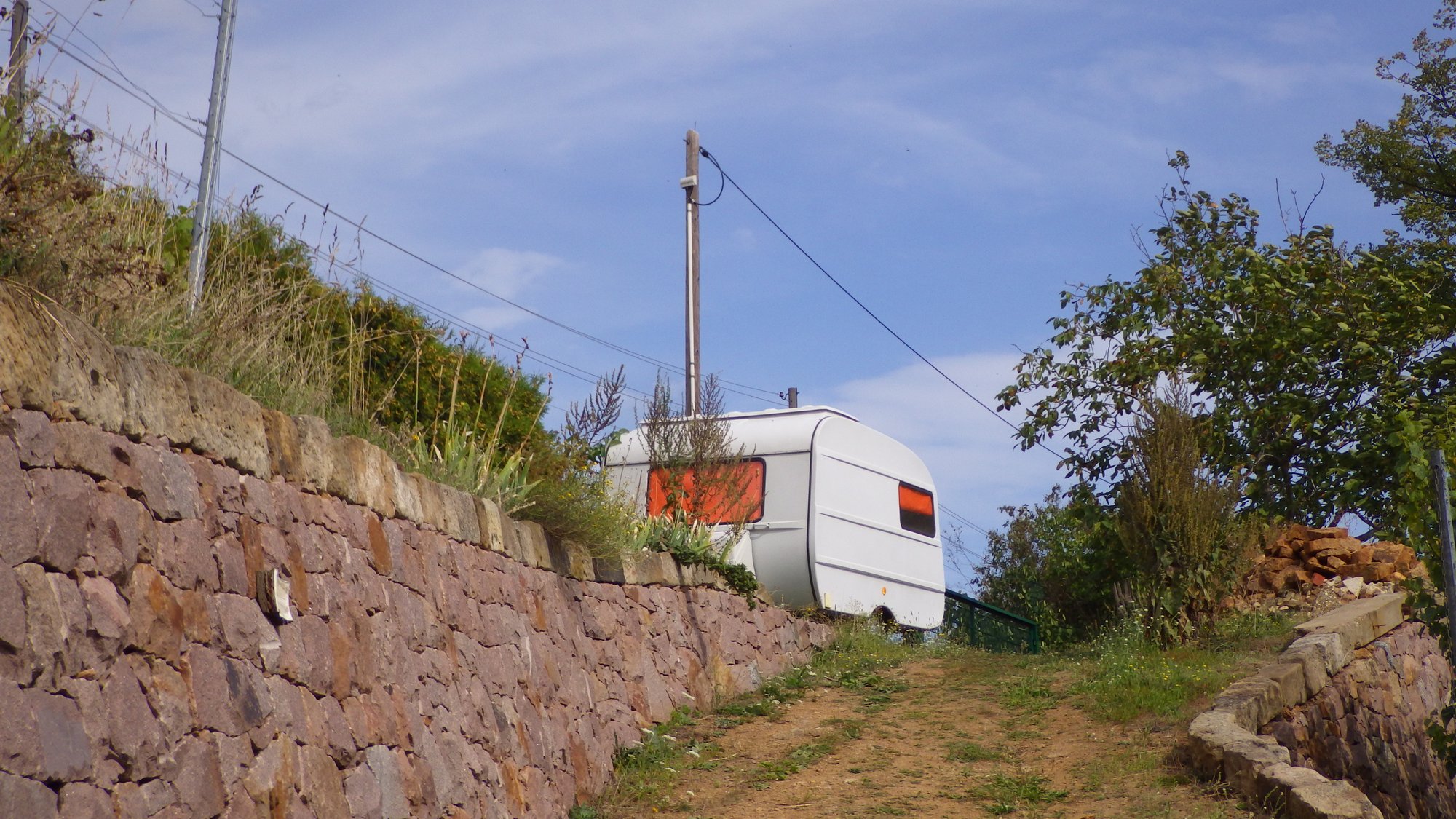 Bright sky, a stone wall, and an old camping trailer parked mostly in the middle of the picture.